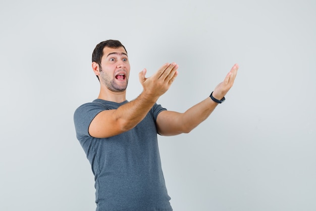 Jovem homem com uma camiseta cinza convidando a vir e parecendo jovial