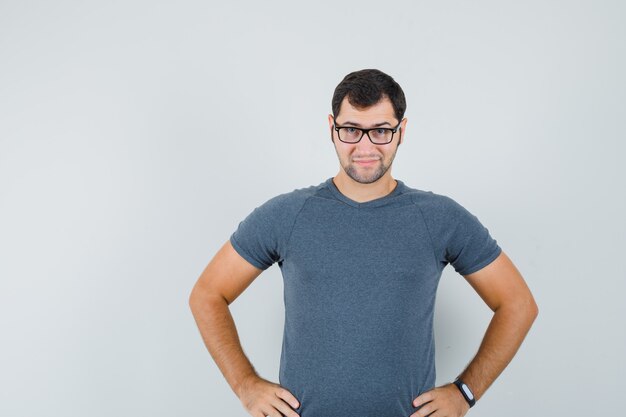 Jovem homem com uma camiseta cinza de mãos dadas na cintura e parecendo inteligente