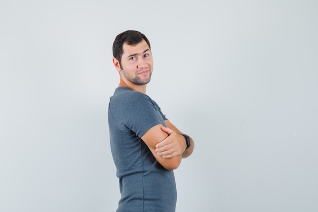 Foto grátis jovem homem com uma camiseta cinza em pé com os braços cruzados e com ar positivo