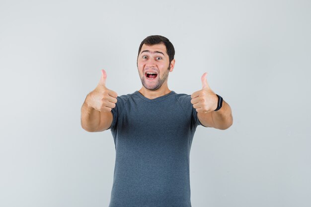 Jovem homem com uma camiseta cinza mostrando dois polegares para cima e parecendo alegre