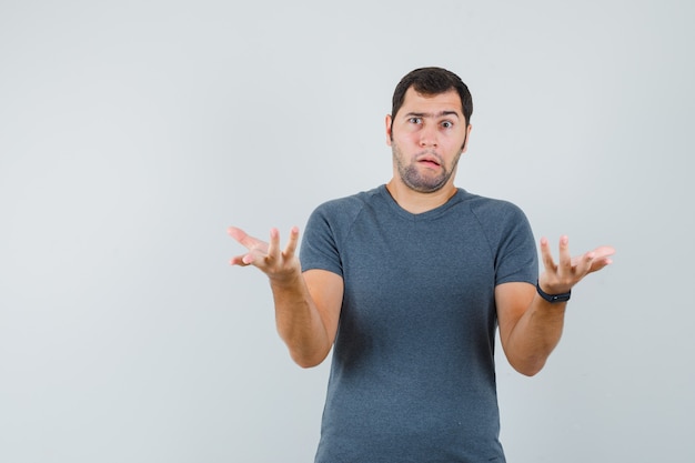 Jovem homem com uma camiseta cinza mostrando um gesto desamparado e parecendo confuso