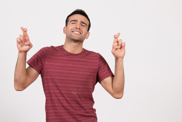 Jovem homem com uma camiseta vermelha escura cruzando os dedos sobre um fundo branco de frente