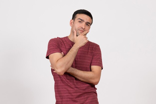 Jovem homem com uma camiseta vermelha escura em pé e posando em um fundo branco de frente