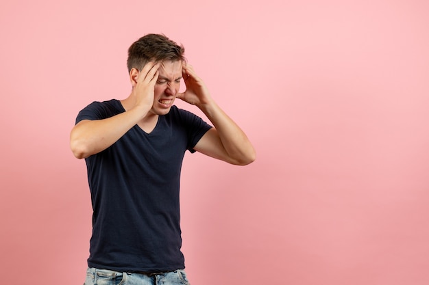 Jovem homem de camisa azul escura com dor de cabeça em fundo rosa de emoção humana homem de cor de frente