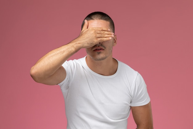 Foto grátis jovem homem de camisa branca estressado cobrindo o rosto em fundo rosa