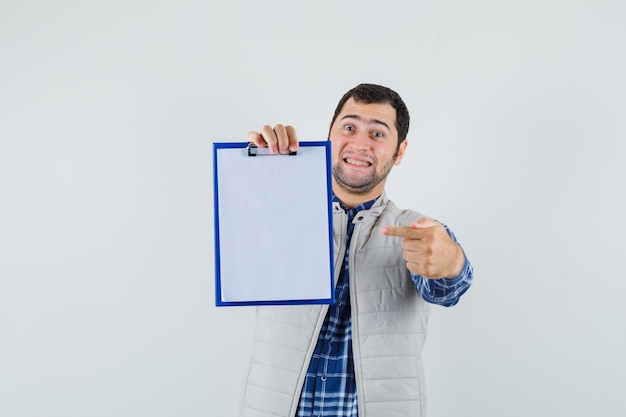 Jovem homem de camisa, jaqueta, apontando para a área de transferência em branco e parecendo satisfeito, vista frontal.