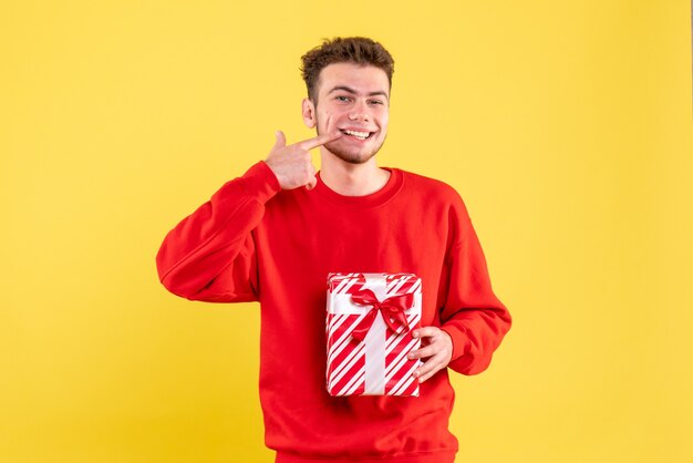 Jovem homem de camisa vermelha e presente de Natal sorrindo de frente