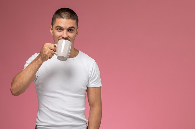 Jovem homem de camiseta branca bebendo café no fundo rosa