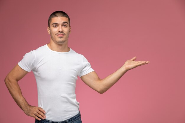 Jovem homem de camiseta branca, de frente para a frente, posando com a mão levantada e a palma da mão no fundo rosa