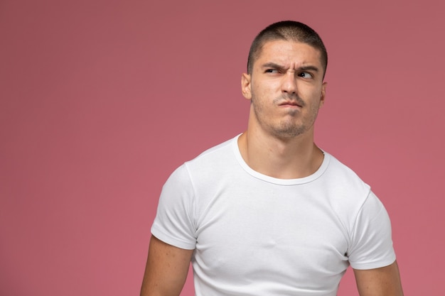 Jovem homem de camiseta branca, de frente para a frente, posando com expressão cética no fundo rosa