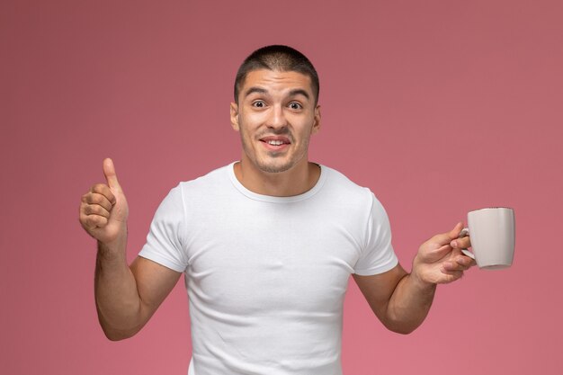 Jovem homem de camiseta branca segurando uma xícara de café no fundo rosa