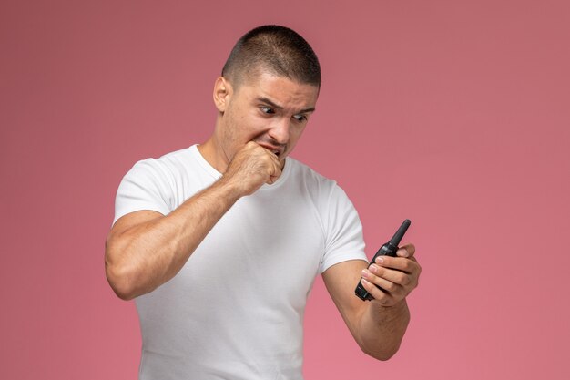 Jovem homem de camiseta branca usando walkie-talkie com expressão de raiva na mesa rosa