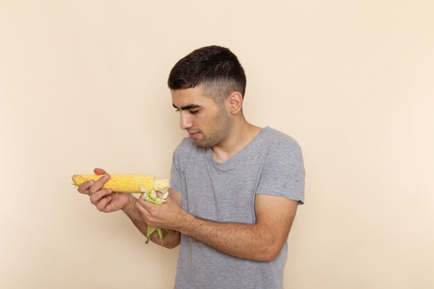 Jovem homem de camiseta cinza segurando milho cru na frente