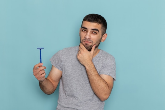 Foto grátis jovem homem de camiseta cinza segurando uma lâmina de barbear e pensando no azul de frente