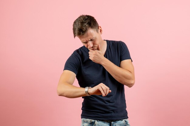 Jovem homem de camiseta escura, de frente para o outro, olhando para o pulso em um fundo rosa