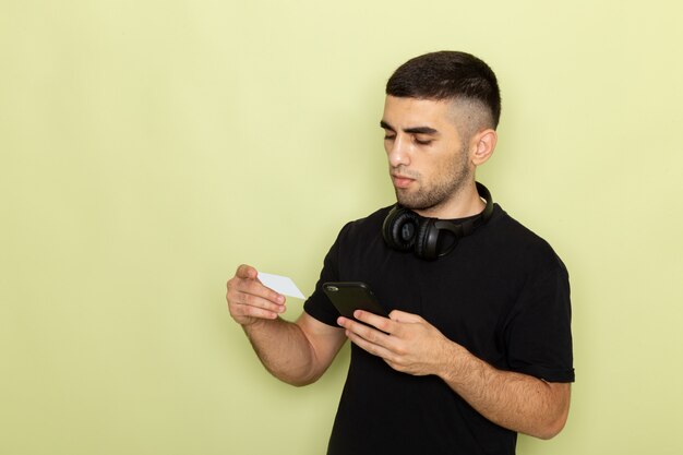 Jovem homem de camiseta preta segurando um cartão branco e usando um telefone verde