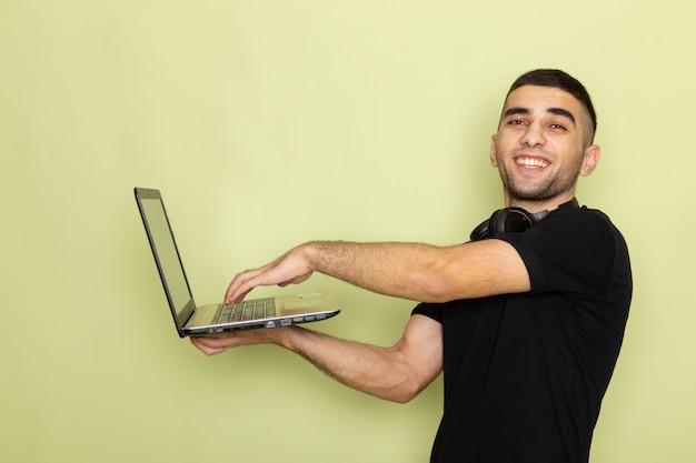 Foto grátis jovem homem de camiseta preta sorrindo e usando laptop forte na frente