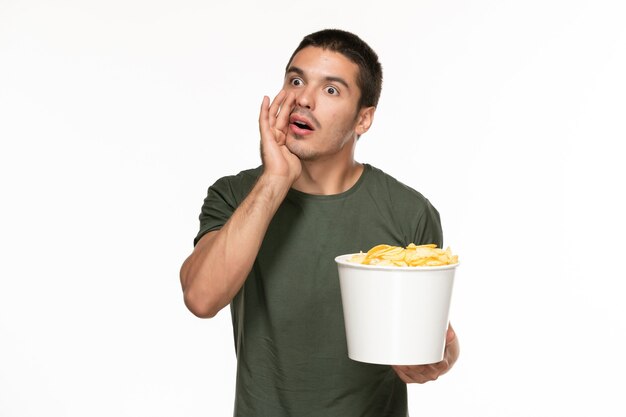 Jovem homem de camiseta verde segurando a cesta com batata cip e comendo na parede branca filme prazer solitário