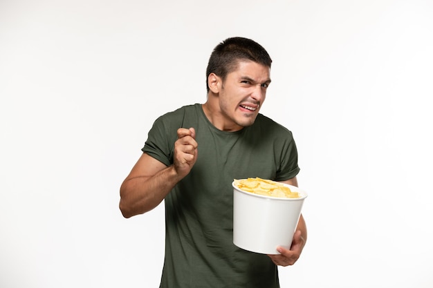 Jovem homem de camiseta verde segurando batata cips de frente assistindo filme na parede branca filme filme de pessoa solitária