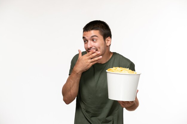 Jovem homem de camiseta verde segurando batata cips e rindo na parede branca filme solitário cinema pessoa de frente