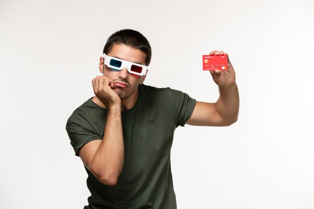 Jovem homem de camiseta verde segurando o cartão do banco vermelho em óculos de sol na parede branca filme de cinema solitário vista frontal