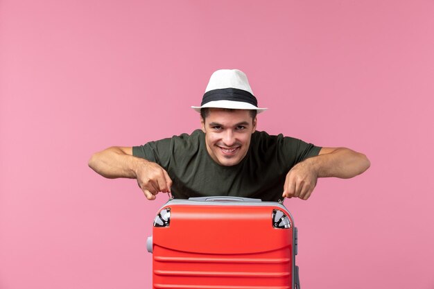 Jovem homem de férias de frente com bolsa vermelha sorrindo no espaço rosa