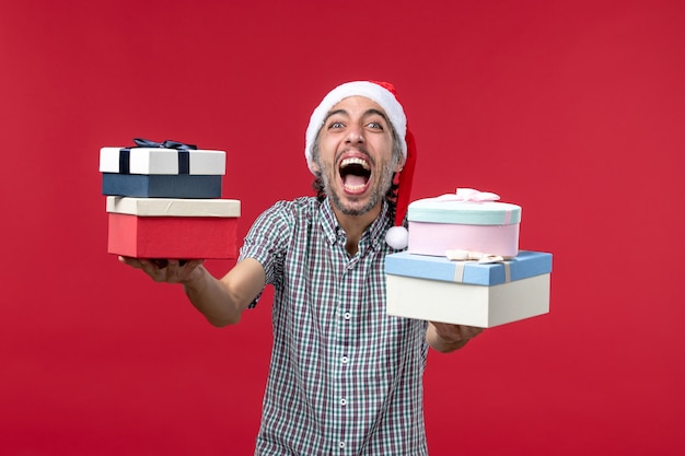 Foto grátis jovem homem de frente feliz segurando presentes em fundo vermelho