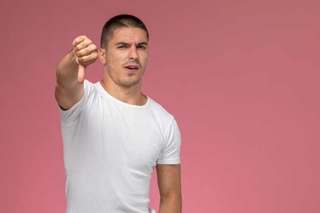 Jovem homem de frente para uma camiseta branca mostrando sinal diferente no fundo rosa