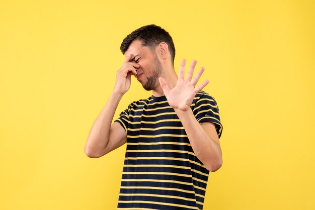 Jovem homem de frente para uma camiseta listrada em preto e branco, segurando a cabeça em um fundo amarelo isolado