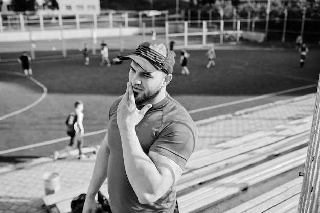 Jovem homem musculoso barbudo brutal usa shorts de camisa vermelha e boné no estádio