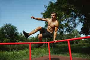 Foto grátis jovem homem musculoso sem camisa caucasiano pulando acima da barra horizontal no playground em um dia ensolarado de verão. treinar a parte superior do corpo ao ar livre. conceito de esporte, treino, estilo de vida saudável, bem-estar.