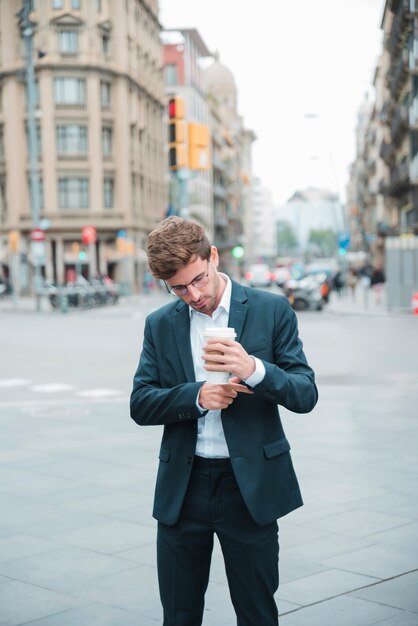 Jovem, homem negócios fica, ligado, rua, segurando, xícara café, em, mão, ajustar, seu, manga