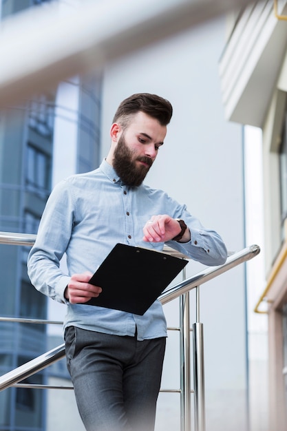 Jovem, homem negócios, segurando clipboard, em, mão, tempo verificando