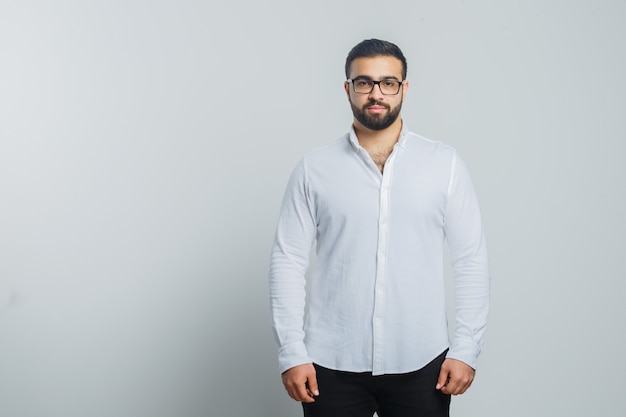 Foto grátis jovem homem olhando para a câmera de camisa branca, calça e bonito