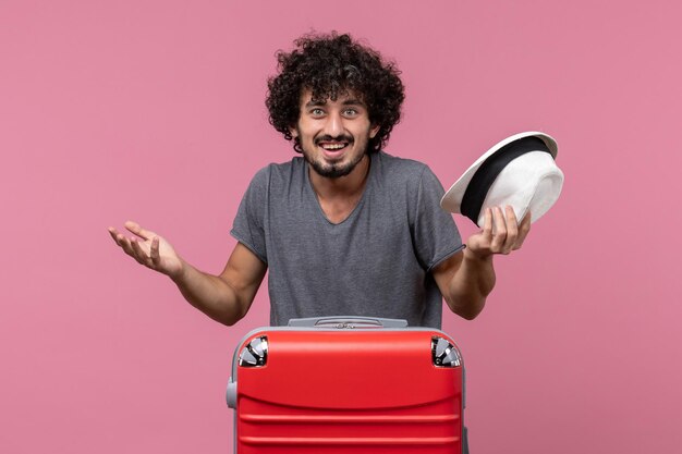 Jovem homem se preparando para as férias segurando um chapéu no espaço rosa