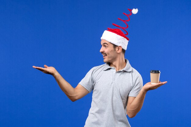 Jovem homem segurando a xícara de café na parede azul com emoções de ano novo masculino