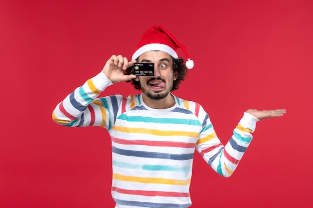 Jovem homem segurando o cartão do banco na parede vermelha vermelho masculino nas emoções do feriado de frente