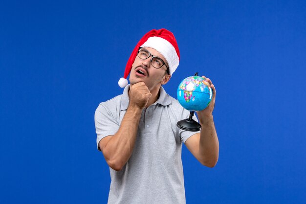 Jovem homem segurando o globo terrestre de frente na parede azul, viagem de avião humano