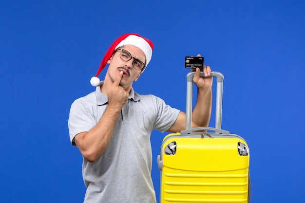 Jovem homem segurando um cartão de banco amarelo em uma viagem de emoção de fundo azul de frente