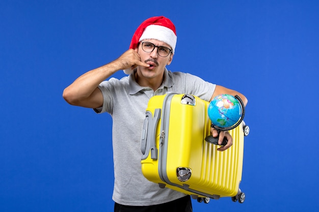 Jovem homem segurando um globo e uma bolsa amarela em uma viagem de férias de avião de parede azul