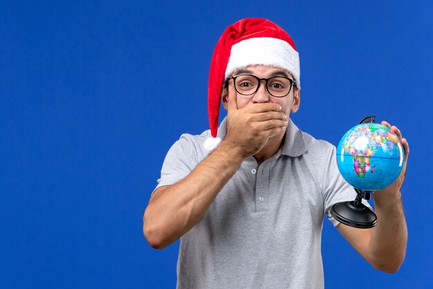 Jovem homem segurando um globo terrestre em uma viagem de férias de avião humano de parede azul