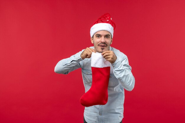 Jovem homem segurando uma meia de natal no chão vermelho, vista frontal, natal, feriado, natal