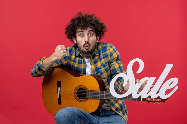 Foto grátis jovem homem sentado com a guitarra na parede vermelha venda de frente tocar música cor aplausos músico ao vivo