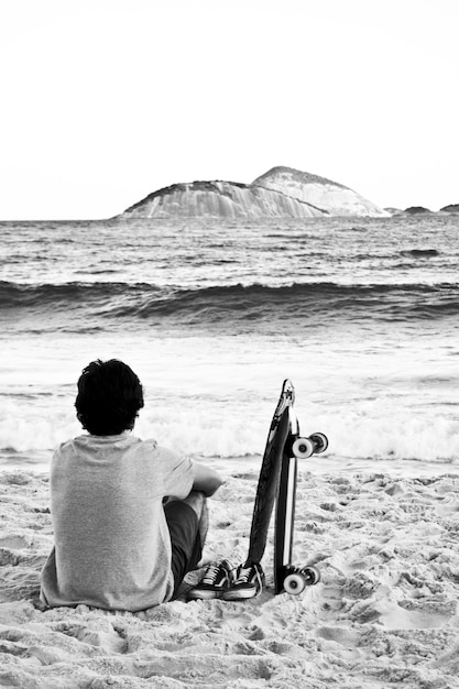 Jovem homem sentado em uma praia admirando o mar