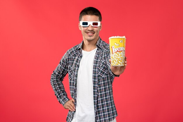 Foto grátis jovem homem sorrindo e segurando um pacote de pipoca em óculos de sol de frente em um filme de cinema de teatro de parede vermelho claro