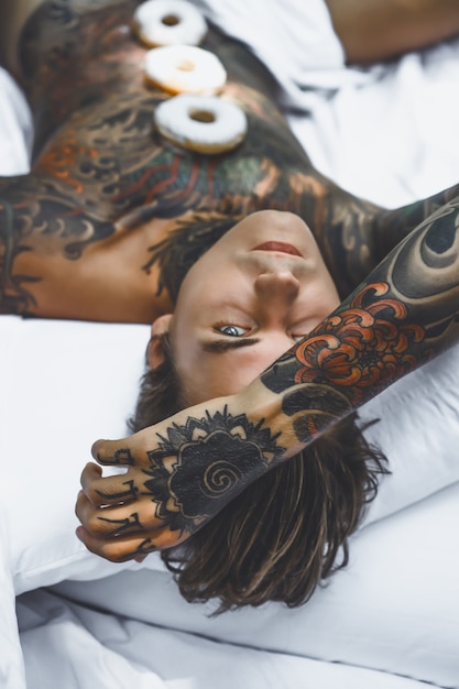 Jovem homem tatuado bonito tomando café da manhã na cama ao ar livre ao ar livre no jardim