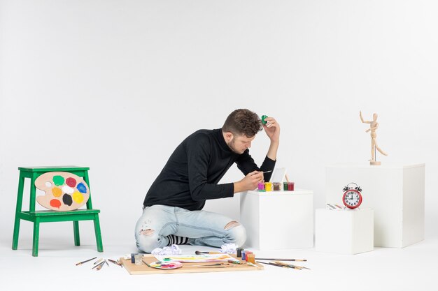 Jovem homem trabalhando com tintas na parede branca pintar arte colorida artista pintando desenho de foto de frente