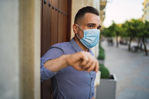 Jovem homem vestindo uma camisa azul em pé no portão com uma máscara facial médica