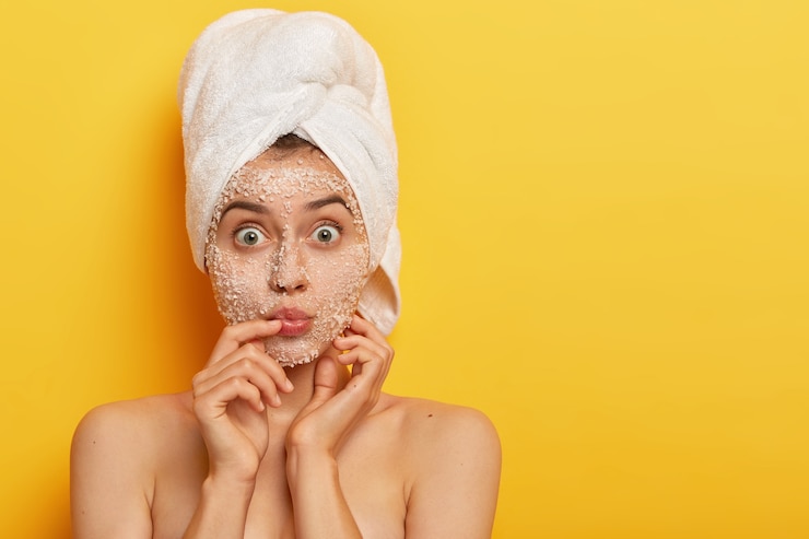 Foto grátis jovem impressionada mantém os lábios arredondados, tem os olhos bem abertos, passa esfoliante com sal marinho, usa toalha enrolada na cabeça, tem pele delicada e macia, modelos indoor. pessoas, spa, peeling, conceito de frescor