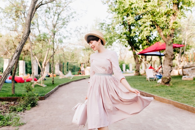 Foto grátis jovem incrível brincando com seu vestido longo roxo claro, caminhando no beco do parque antes de um piquenique com os amigos